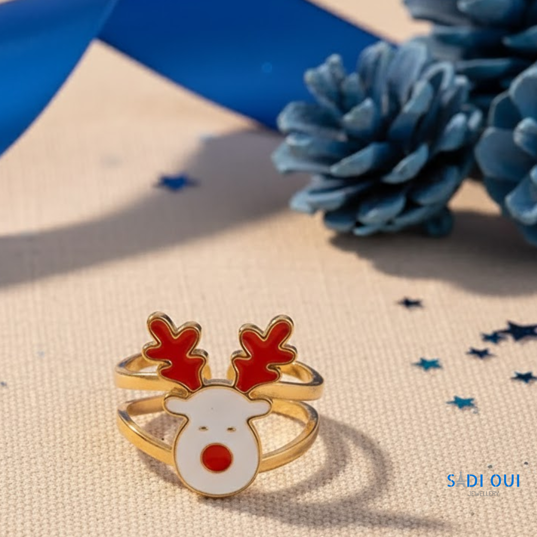 Anel Rena Christmas Fun dourado com rena branca e vermelha em fundo bege com estrelas azuis