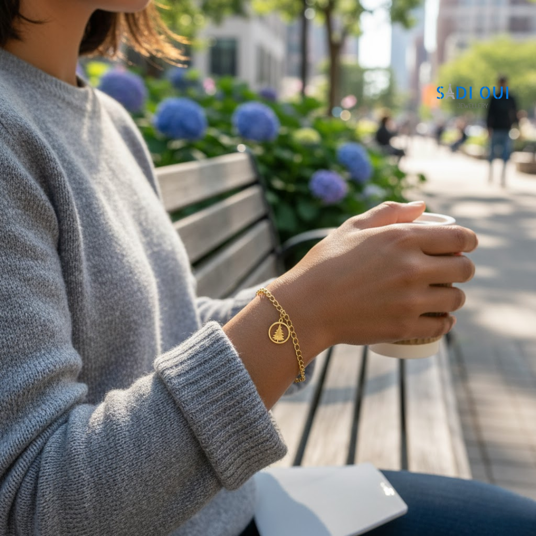 Pessoa a usar a Pulseira Árvore de Natal Winter Magic dourada, sentada num banco de jardim com uma chávena na mão