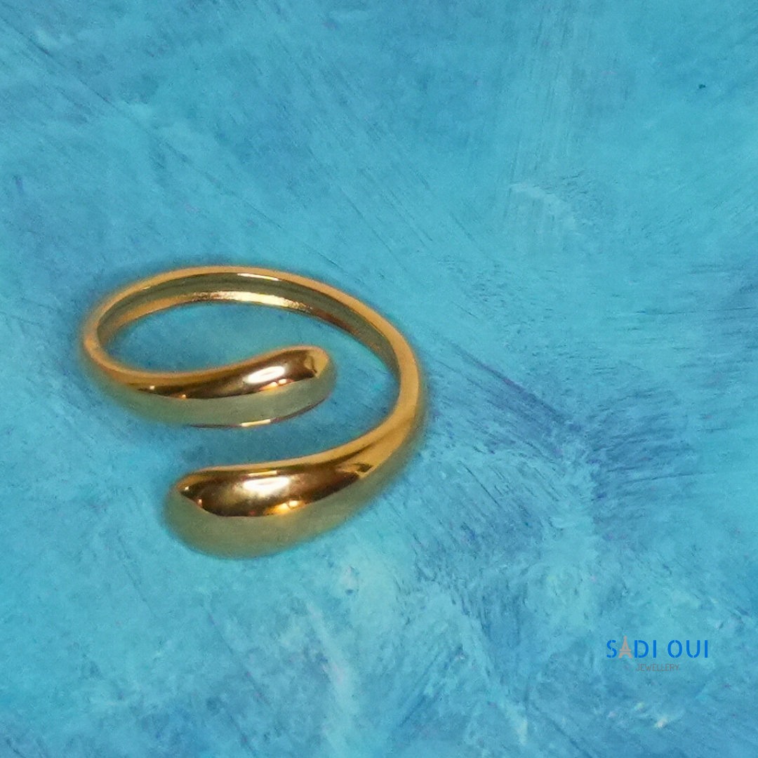 Anel Pop Drop em aço inoxidável dourado em fundo azul
