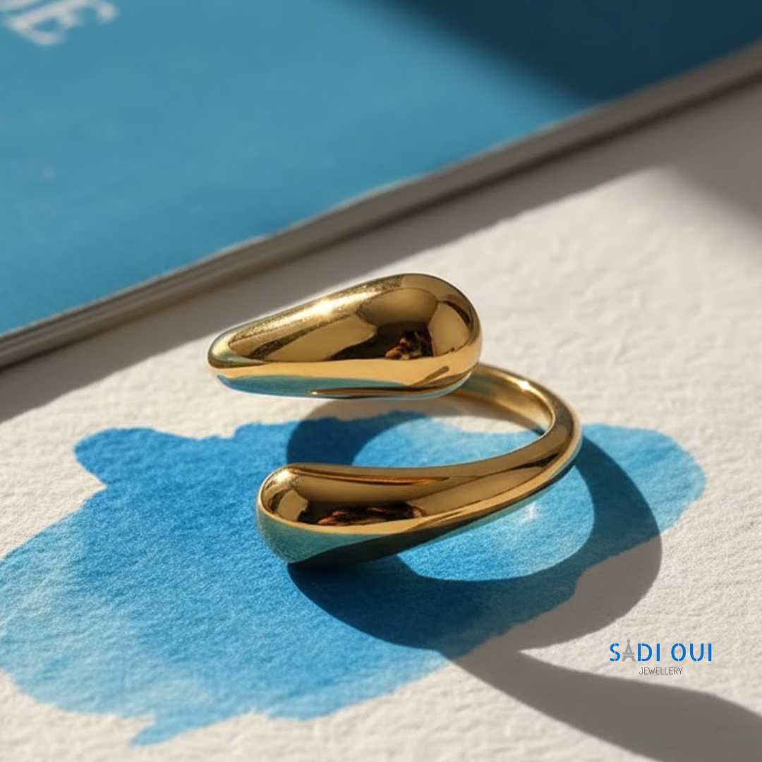 Anel Pop Drop em aço inoxidável dourado em fundo claro com mancha azul
