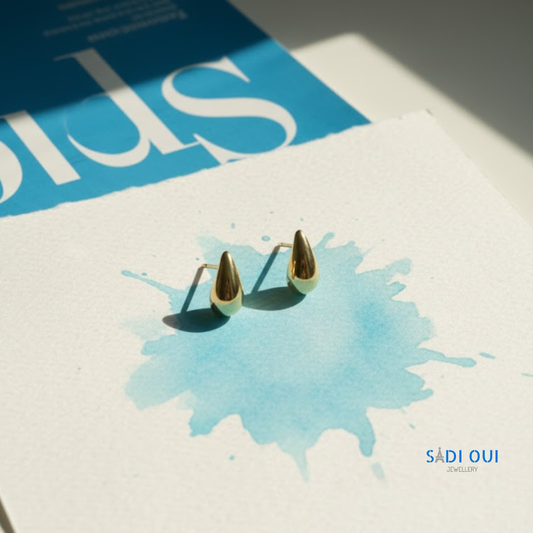 Brincos Pop Drop em aço inoxidável dourado em fundo claro com mancha azul
