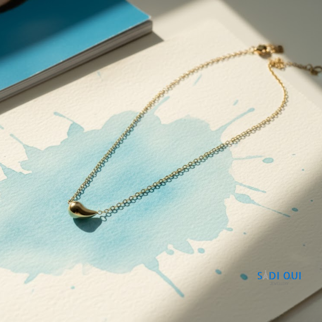 Colar Pop Drop em aço inoxidável dourado em fundo claro com mancha azul
