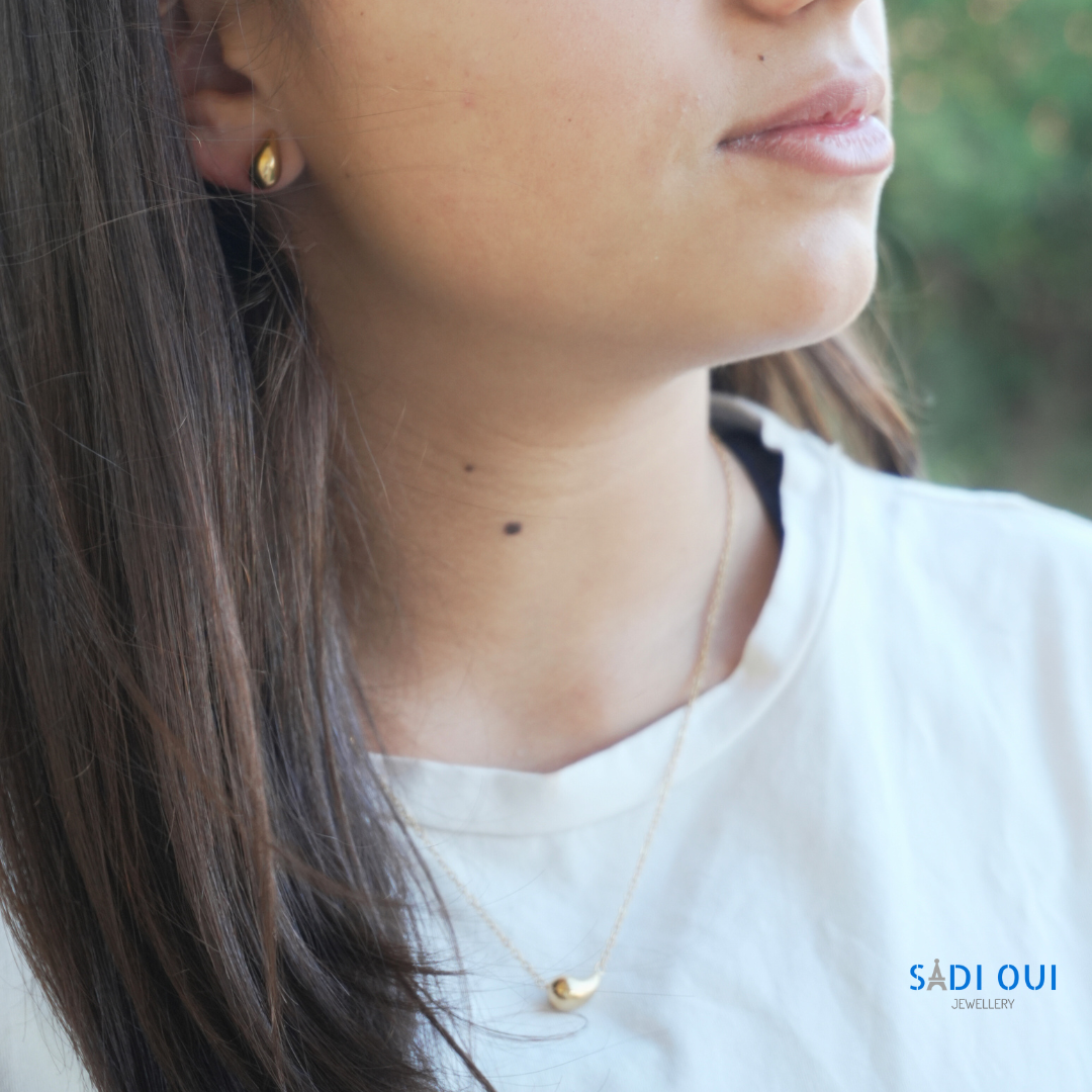 Colar Pop Drop em aço inoxidável dourado no pescoço de uma pessoa com t shirt branca
