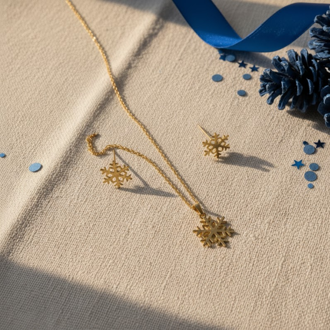 Conjunto Floco de Neve Winter Magic com colar e brincos dourados sobre fundo bege com detalhes azuis, joias de Natal SADI OUI Jewellery
