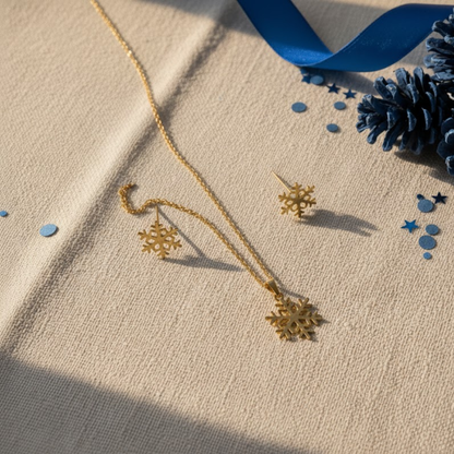 Conjunto Floco de Neve Winter Magic com colar e brincos dourados sobre fundo bege com detalhes azuis, joias de Natal SADI OUI Jewellery
