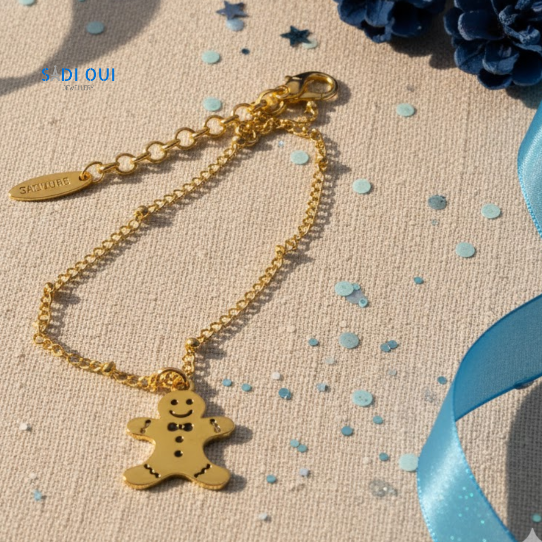 Pulseira Gingerbread Winter Magic dourada com pendente de boneco de gengibre em fundo bege com confetis azuis
