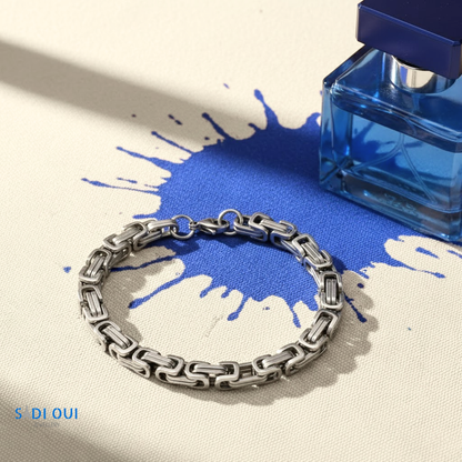 Pulseira Masculina Base em aço inoxidável prateado em fundo bege e azul com frasco de perfume azul
