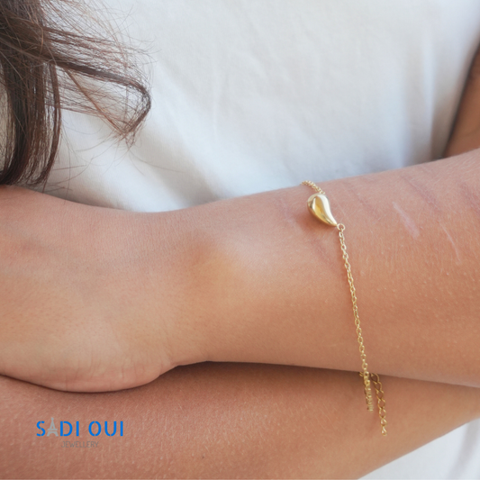 Pulseira Pop Drop em aço inoxidável dourado no pulso de uma pessoa com t shirt branca
